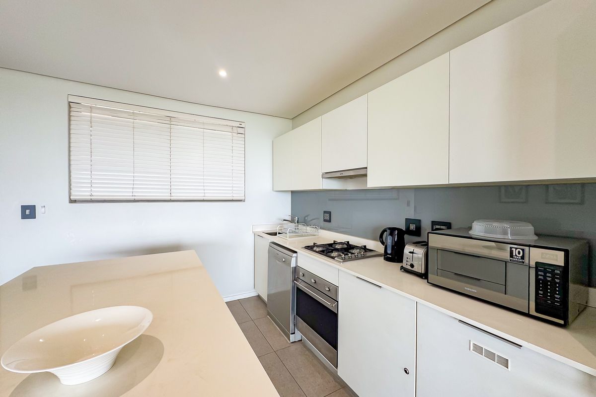 Modern kitchen featuring sleek white cabinetry, stone countertops, integrated appliances, gas hob, and a glass splashback with neutral tiled flooring.