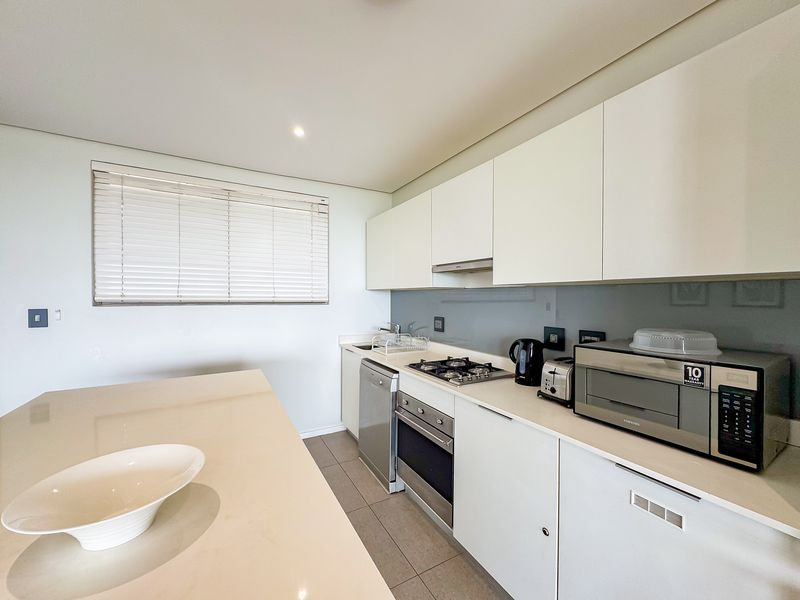 Modern kitchen featuring sleek white cabinetry, stone countertops, integrated appliances, gas hob, and a glass splashback with neutral tiled flooring.