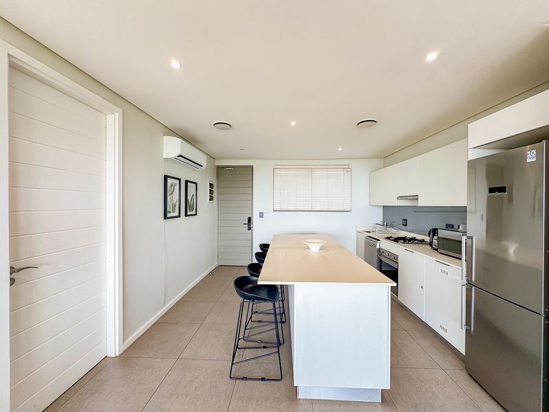 Modern kitchen featuring a central island, sleek white cabinetry, integrated appliances, recessed lighting, and neutral tiled flooring in an open-plan layout.
