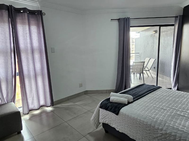 A bedroom featuring tiled flooring, built-in cupboards, and a sliding glass door providing access to an outdoor balcony area.