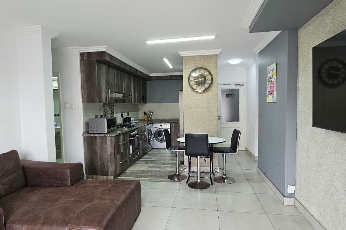 An open-plan living and kitchen area featuring modern cabinetry, granite countertops, tiled flooring, and a textured feature wall, creating a functional and cohesive living space.