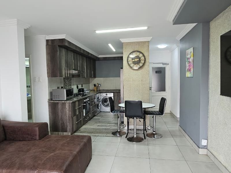 An open-plan living and kitchen area featuring modern cabinetry, granite countertops, tiled flooring, and a textured feature wall, creating a functional and cohesive living space.