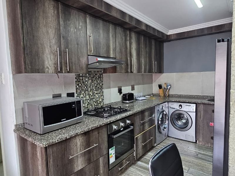 A functional kitchen featuring dark wood-look cabinetry, granite countertops, a mosaic backsplash, and integrated laundry appliances.