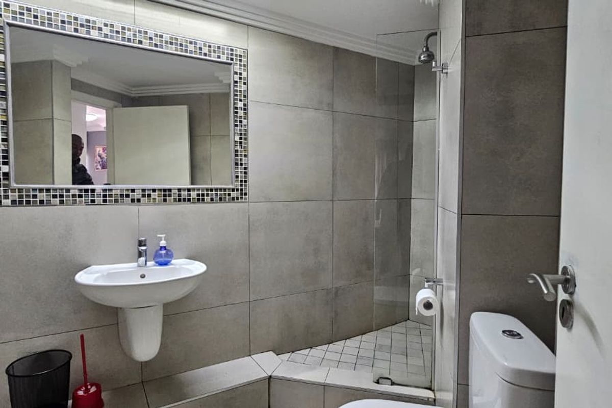 Modern bathroom featuring large format wall tiles, a wall-mounted basin, a glass-enclosed shower, and a toilet.