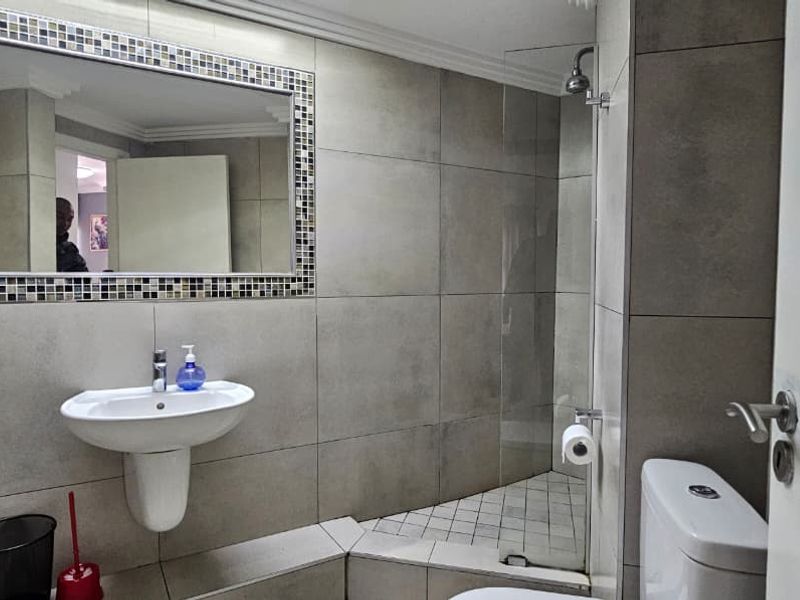 Modern bathroom featuring large format wall tiles, a wall-mounted basin, a glass-enclosed shower, and a toilet.