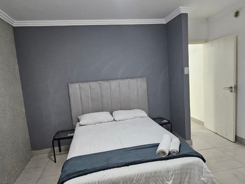 A simple bedroom featuring tiled flooring, crown molding, and a neutral grey accent wall.