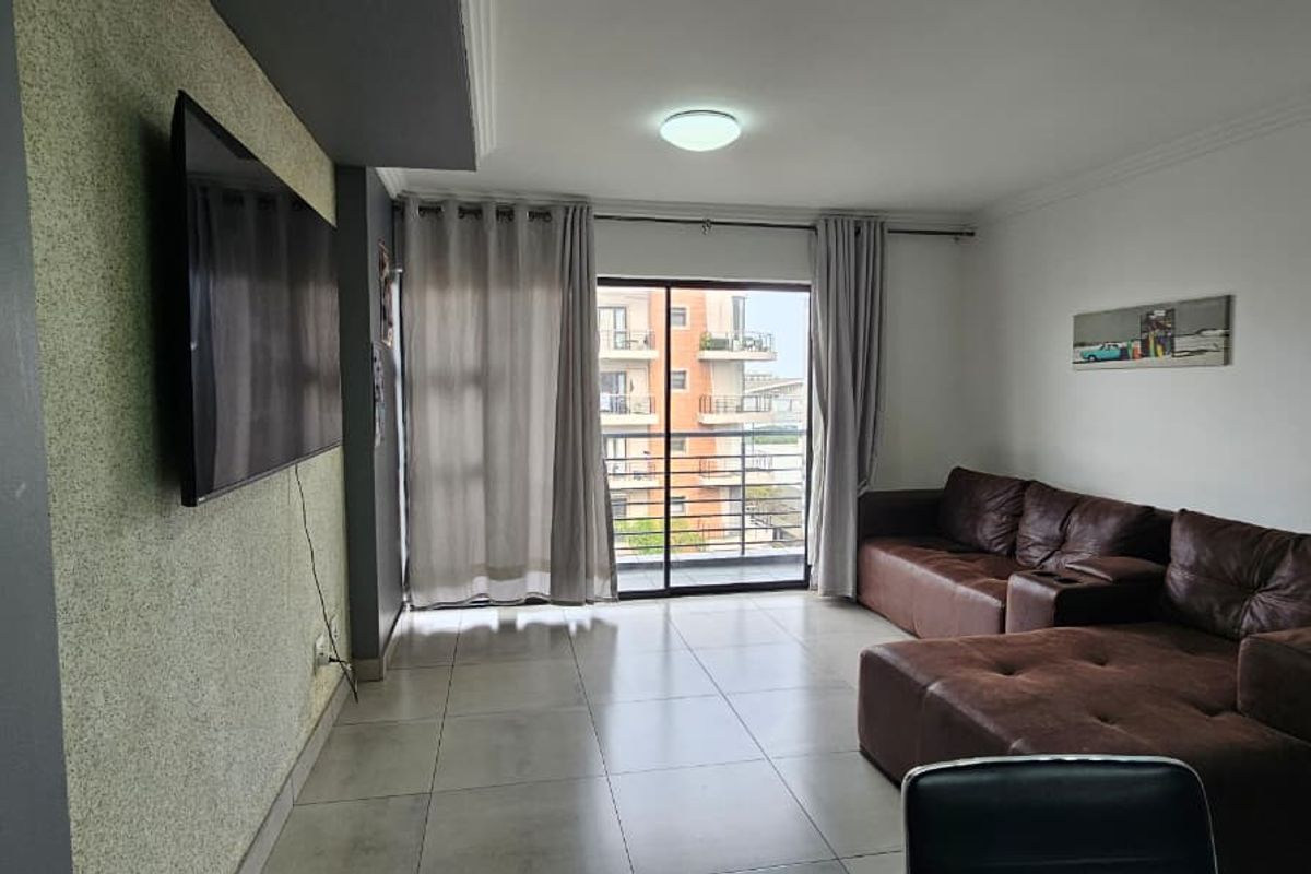 A living room featuring tiled flooring, a textured accent wall, and a sliding glass door leading to a balcony.
