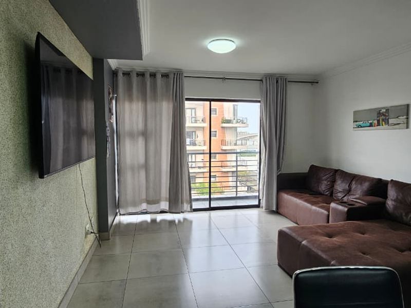 A living room featuring tiled flooring, a textured accent wall, and a sliding glass door leading to a balcony.
