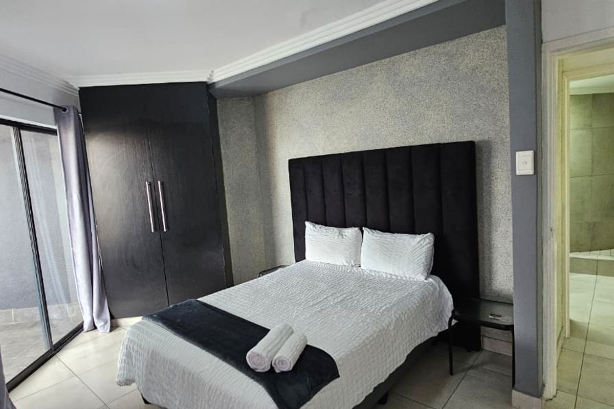 A well-maintained bedroom featuring built-in cupboards, tiled flooring, and an en-suite bathroom with direct access to a balcony through a sliding glass door.