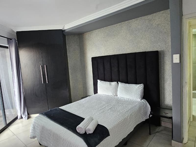 A well-maintained bedroom featuring built-in cupboards, tiled flooring, and an en-suite bathroom with direct access to a balcony through a sliding glass door.