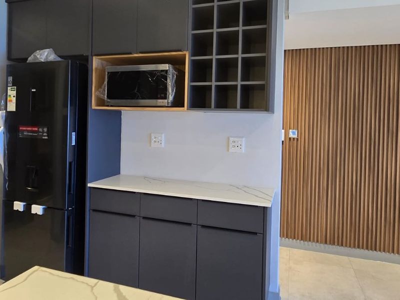 Modern kitchen area featuring dark grey cabinetry, stone countertops, built-in microwave, and decorative slatted wood wall paneling.