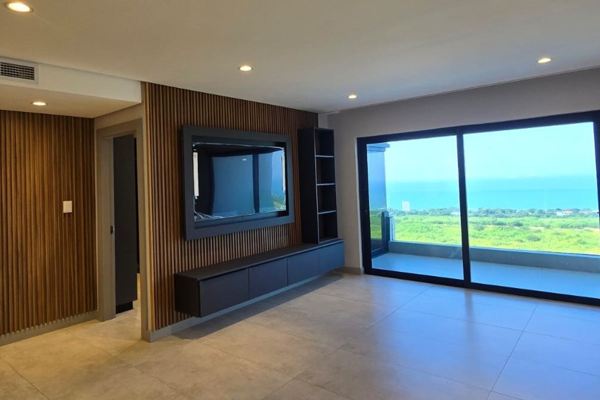 Modern living area featuring elegant slatted timber wall paneling, built-in media cabinetry, large sliding doors, and expansive coastal views.
