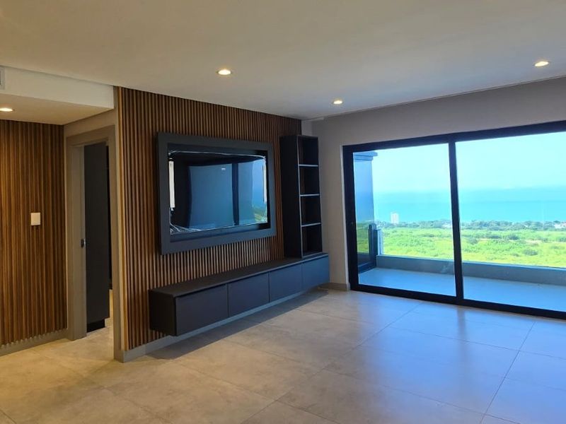 Modern living area featuring elegant slatted timber wall paneling, built-in media cabinetry, large sliding doors, and expansive coastal views.