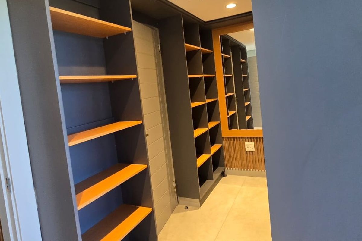 A modern walk-in closet or dressing area featuring extensive built-in shelving, sleek cabinetry, and contemporary slatted wood wall accents.