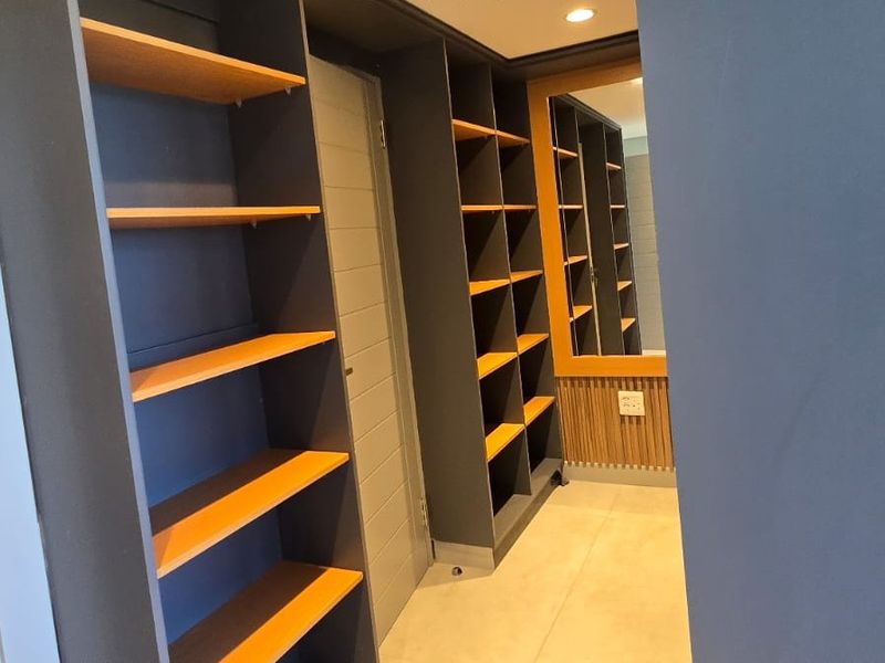 A modern walk-in closet or dressing area featuring extensive built-in shelving, sleek cabinetry, and contemporary slatted wood wall accents.