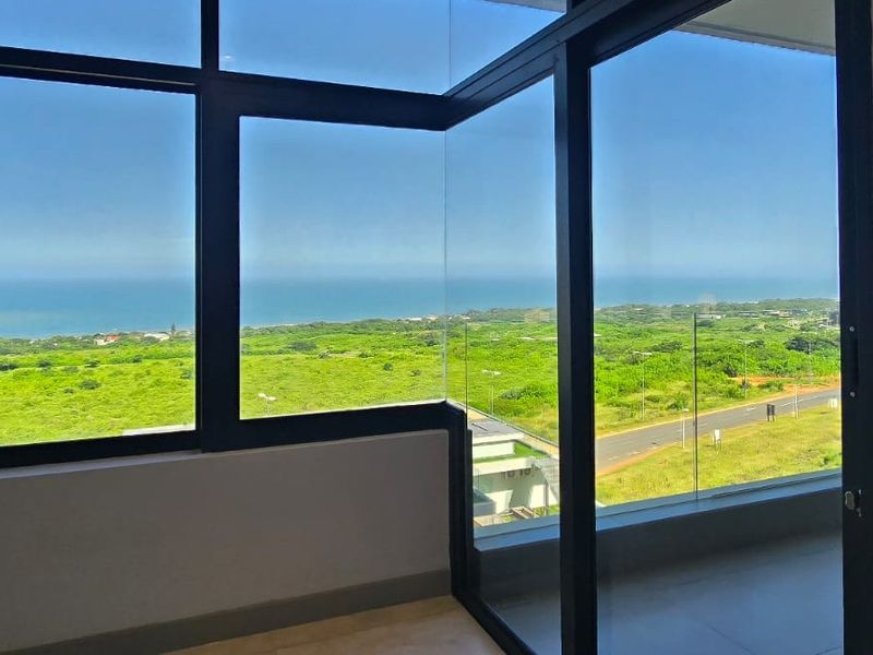 A bright interior space featuring expansive floor-to-ceiling windows with panoramic coastal and landscape views, framed by modern black aluminium joinery.