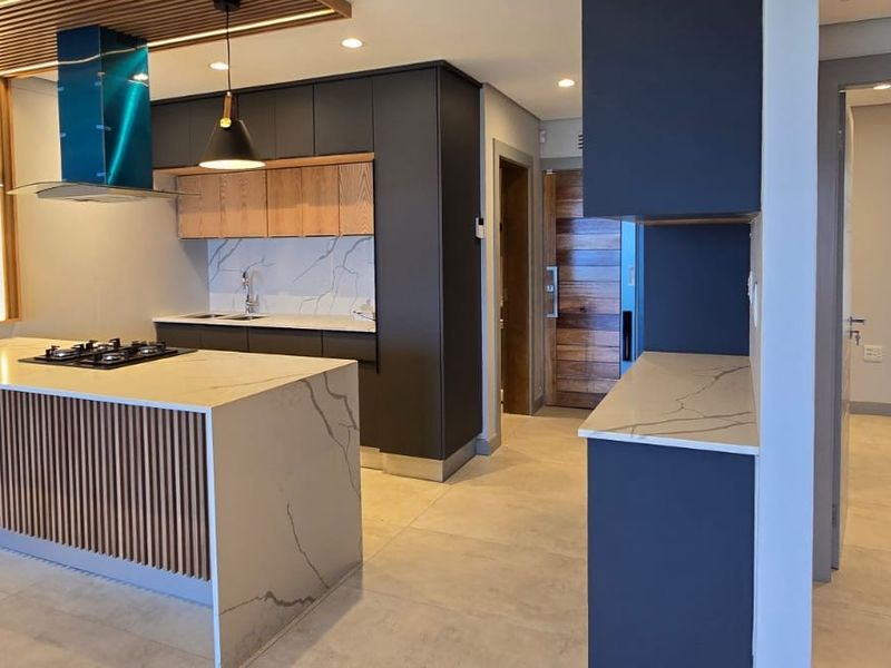 Modern kitchen featuring a stone-topped island with built-in hob, sleek cabinetry, and elegant slatted wood accents, creating a sophisticated and functional culinary space.
