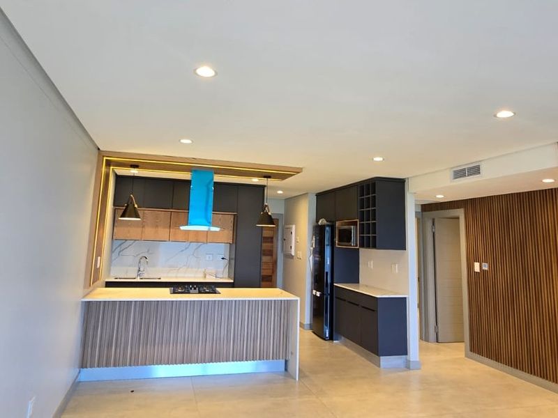 Modern open-plan living area featuring a sleek kitchen with stone countertops, gas hob, and stylish slatted wood wall paneling throughout the space.