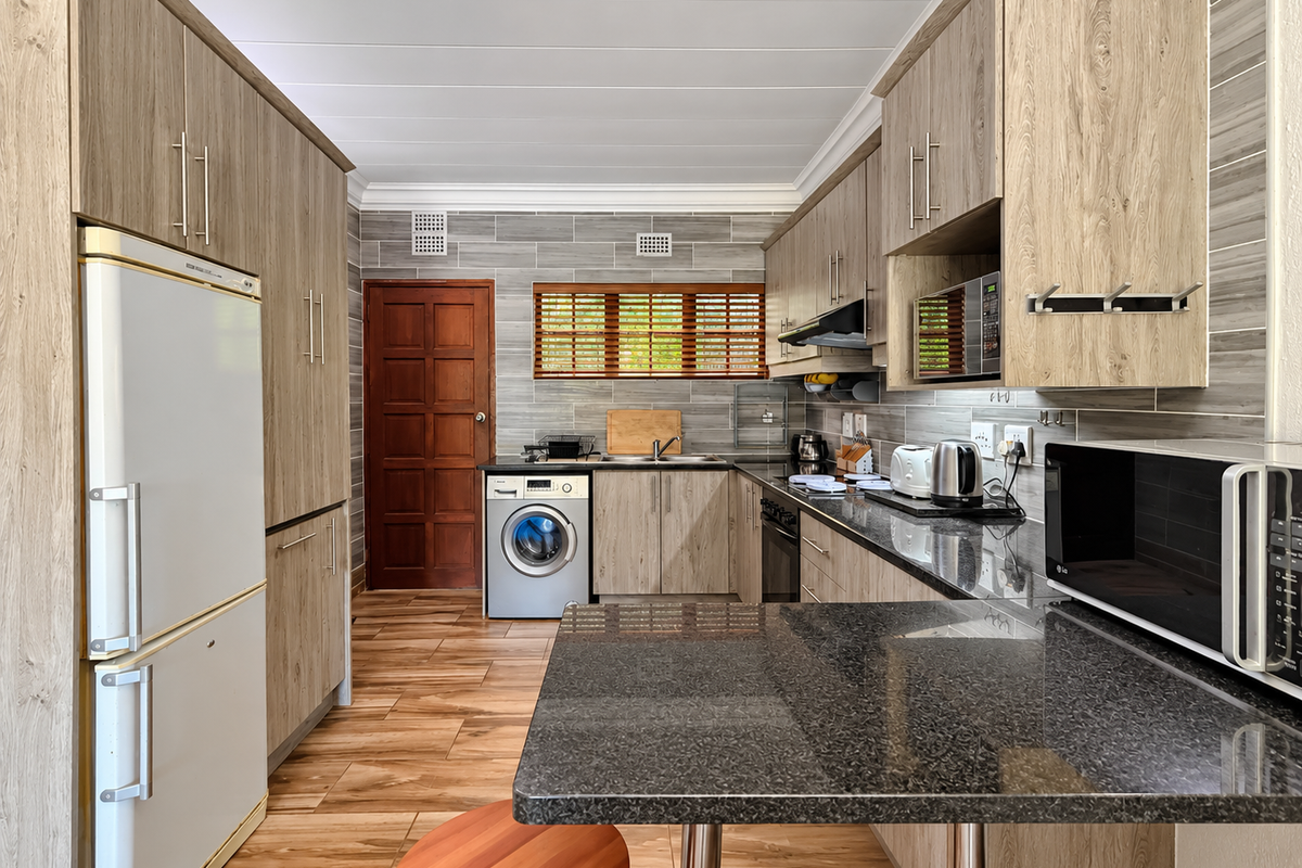 Modern kitchen featuring wood-grain cabinetry, granite countertops, integrated appliances, and tiled finishes, offering a functional and well-maintained culinary space.
