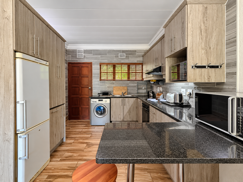 Modern kitchen featuring wood-grain cabinetry, granite countertops, integrated appliances, and tiled finishes, offering a functional and well-maintained culinary space.