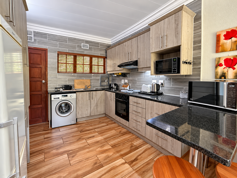 Modern kitchen featuring wood-look cabinetry, granite countertops, integrated appliances, and tiled flooring with a breakfast bar area.
