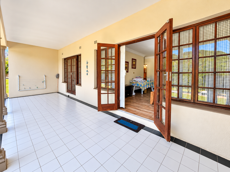 A spacious covered patio featuring white tiled flooring and timber-framed glass doors providing seamless access to the interior living space.