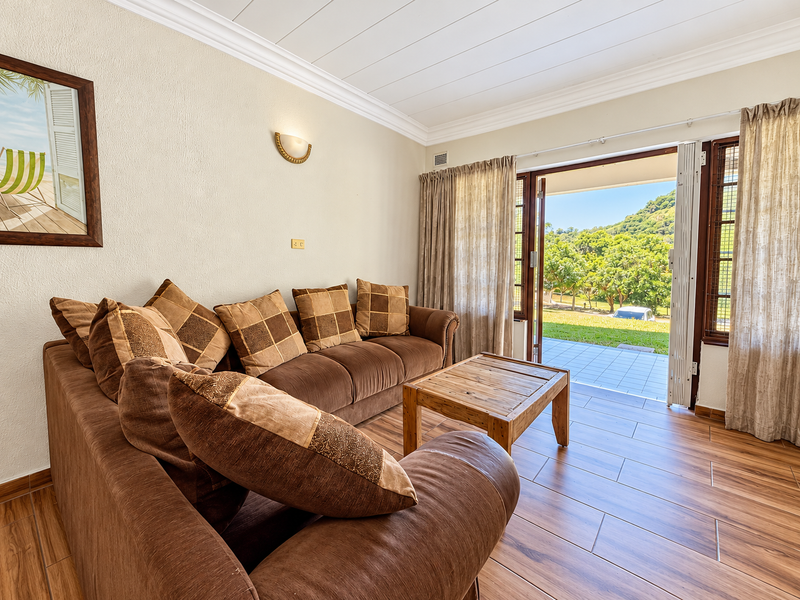 A comfortable living room featuring wood-look tile flooring, crown molding, and a sliding glass door that opens onto a tiled patio with scenic views.