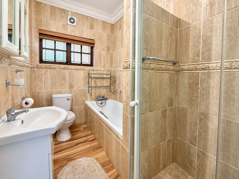 A well-maintained bathroom featuring a vanity basin, toilet, bathtub, and separate shower enclosure with neutral floor-to-ceiling wall tiling.