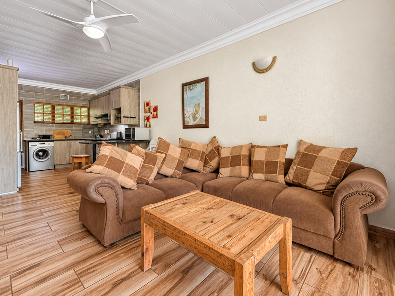 An open-plan living area featuring wood-look tile flooring, a ceiling fan, and a functional kitchen with built-in cabinetry and integrated laundry appliances.