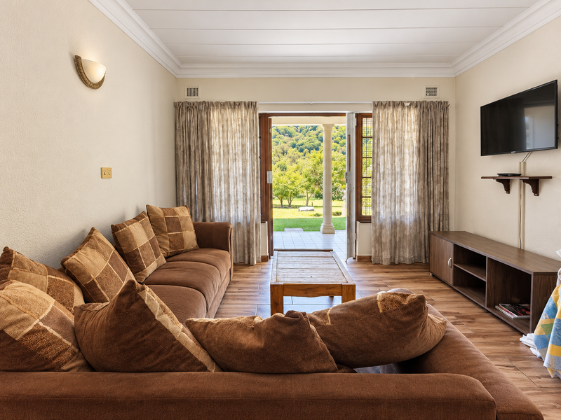 A comfortable living room featuring wood-look tile flooring, crown molding, and direct access to a patio with scenic garden views.