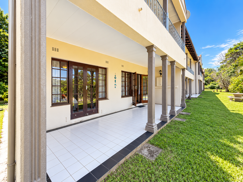 A spacious covered patio featuring tiled flooring, decorative columns, and multiple sets of french doors leading into the apartment.