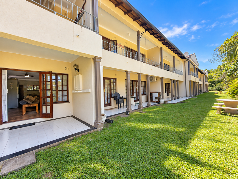 A view of the rear exterior of the apartment building, featuring a series of ground-floor tiled patios and upper-level balconies with support columns.