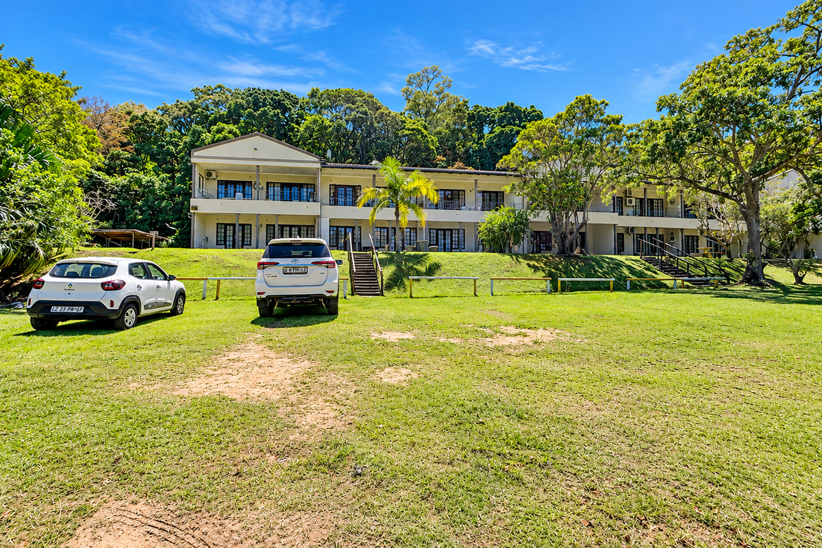 Rear view of a multi-unit apartment complex featuring balconies, sliding doors, and a large shared lawn area with mature trees.