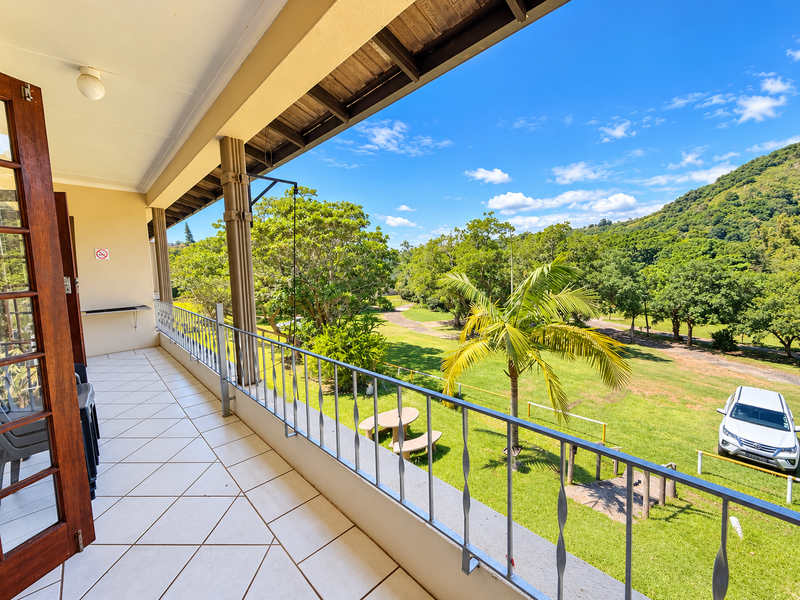 A spacious covered balcony featuring tiled flooring, a metal balustrade, and a timber ceiling, offering scenic views of the surrounding garden and landscape.