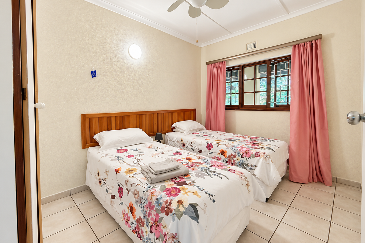 A well-lit bedroom featuring tiled flooring, a wooden headboard, and a ceiling fan, offering a functional and comfortable living space.