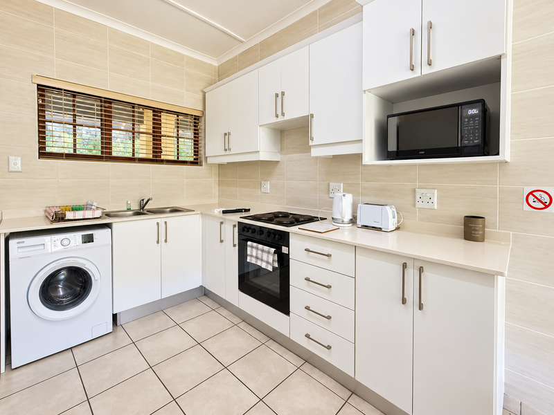 A functional kitchen featuring white cabinetry, stone countertops, integrated oven and hob, and tiled finishes throughout.