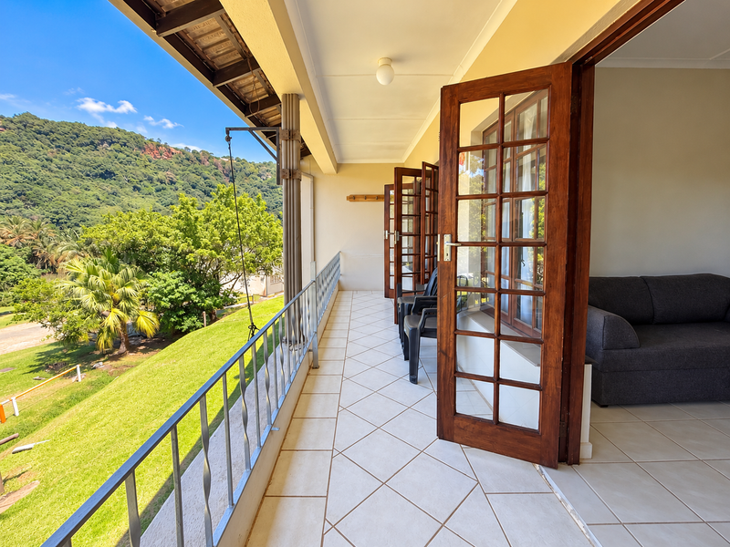 A spacious covered balcony featuring tiled flooring, a metal balustrade, and timber-framed glass doors, offering scenic views of the surrounding landscape.