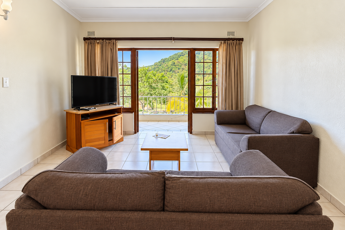 A bright living room featuring tiled flooring and double doors opening onto a balcony with scenic mountain views.
