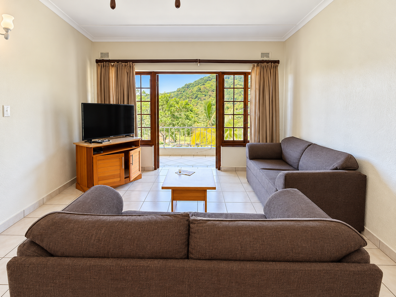 A bright living room featuring tiled flooring and double doors opening onto a balcony with scenic mountain views.