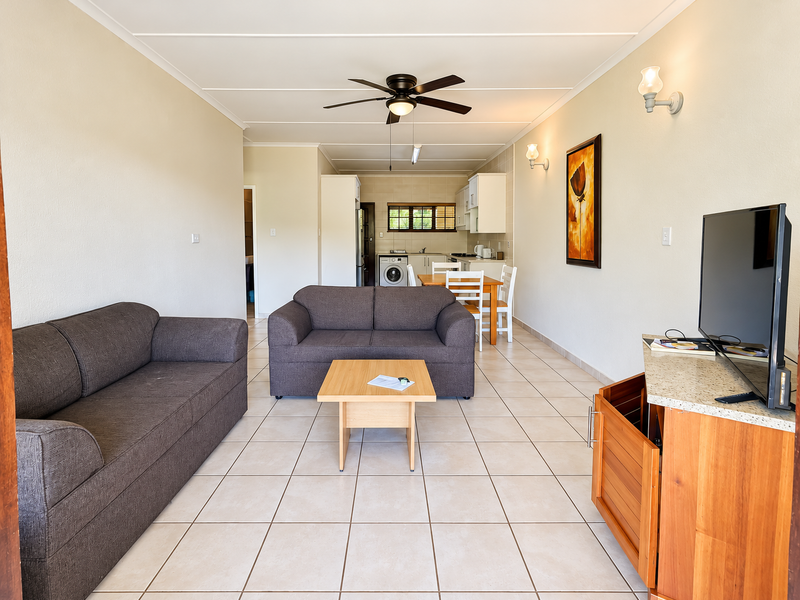 Open-plan living and kitchen area featuring tiled flooring, ceiling fan, and functional kitchen cabinetry with built-in appliances.
