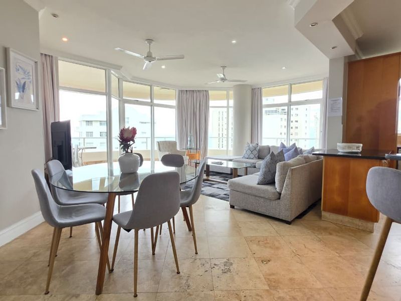Spacious open-plan living and dining area featuring stone tile flooring, recessed lighting, ceiling fans, and large glass doors leading to a balcony.