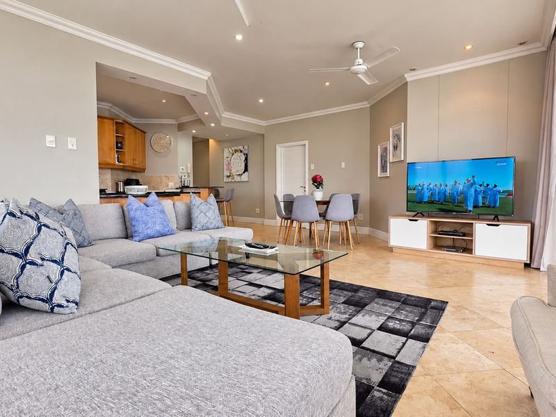 Spacious open-plan living and dining area featuring stone tile flooring, recessed lighting, and a seamless transition to a functional kitchen with breakfast bar.