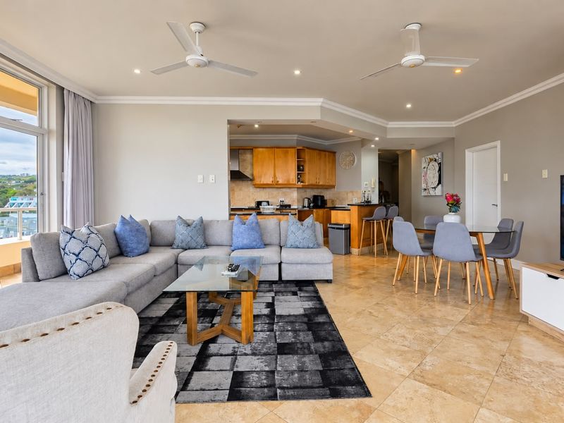 Spacious open-plan living and dining area featuring tiled floors, ceiling fans, and a functional kitchen with built-in cabinetry, flowing onto a balcony with views.