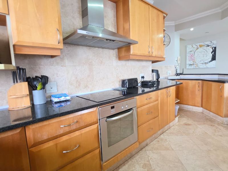 A functional kitchen featuring wooden cabinetry, granite countertops, a built-in oven, electric hob, and a stainless steel extractor fan with tiled finishes.