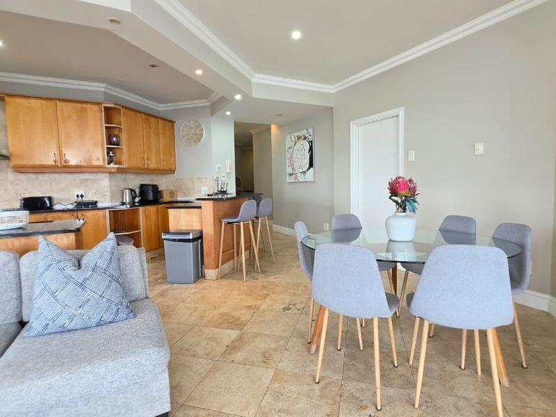 Open-plan living and dining area featuring stone tile flooring, recessed lighting, and a functional kitchen with built-in wooden cabinetry and a breakfast bar.
