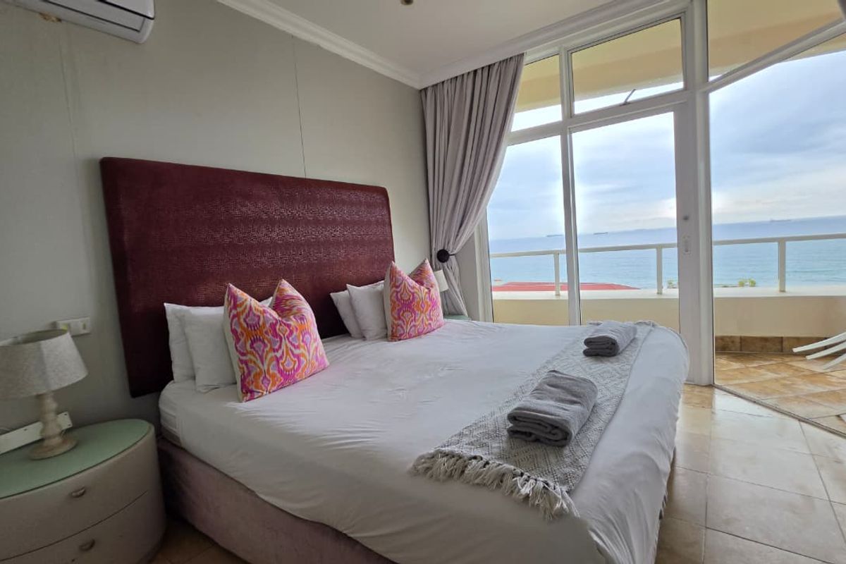 A bright bedroom featuring tiled floors, a split-system air conditioner, and large glass sliding doors that open onto a balcony with ocean views.
