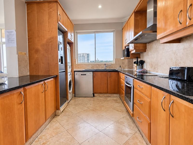 A functional kitchen featuring warm wooden cabinetry, granite countertops, tiled backsplash, and integrated appliances, offering a practical layout with natural light from the window.