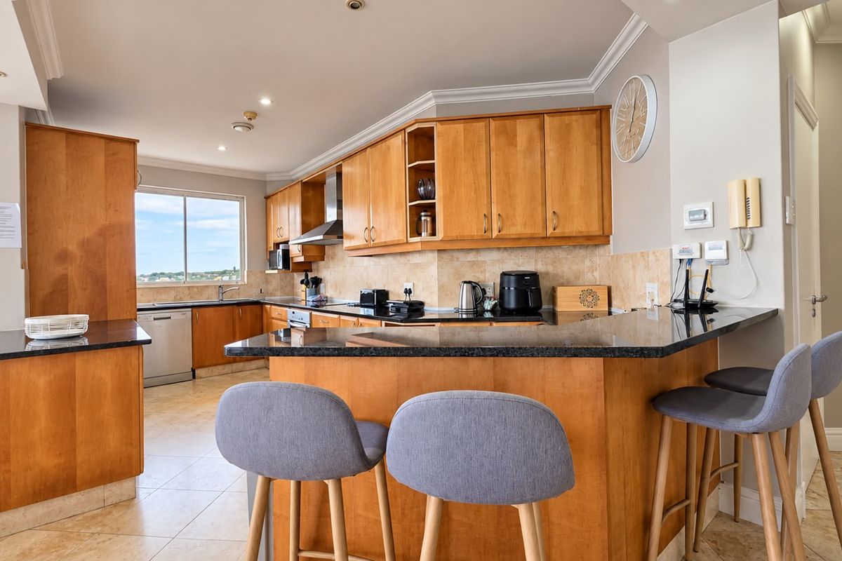A well-maintained kitchen featuring warm wooden cabinetry, granite countertops, a breakfast bar, and integrated appliances, offering a functional and inviting cooking space.