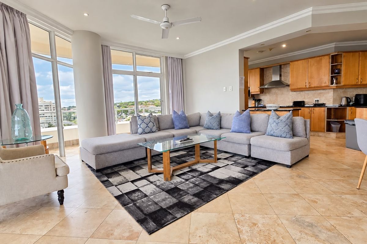 Spacious open-plan living area featuring stone tile flooring, a modern kitchen with wooden cabinetry, and large windows offering expansive views.