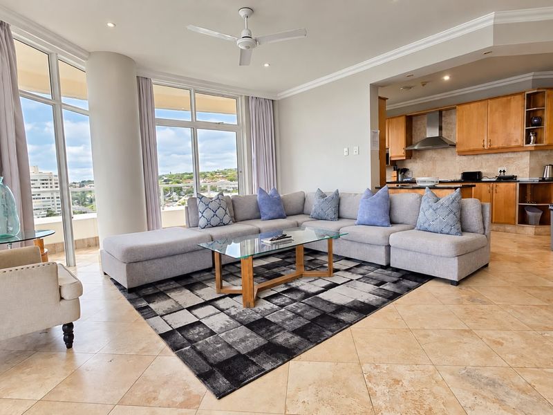 Spacious open-plan living area featuring stone tile flooring, a modern kitchen with wooden cabinetry, and large windows offering expansive views.